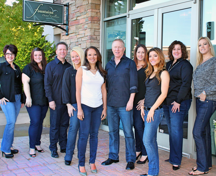 Eight-member, Roseville dentist team, Fountains Dental Excellence, standing outside the front doors of their office, wearing jeans and dress shirts.